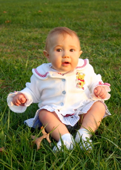 Domino, sitting in a green grass field. She's wearing a white sweater with Winnie the Pooh and a blue and white checkered skirt.