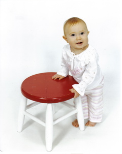 Domino, standing, holding on to a stool with a red top and white legs